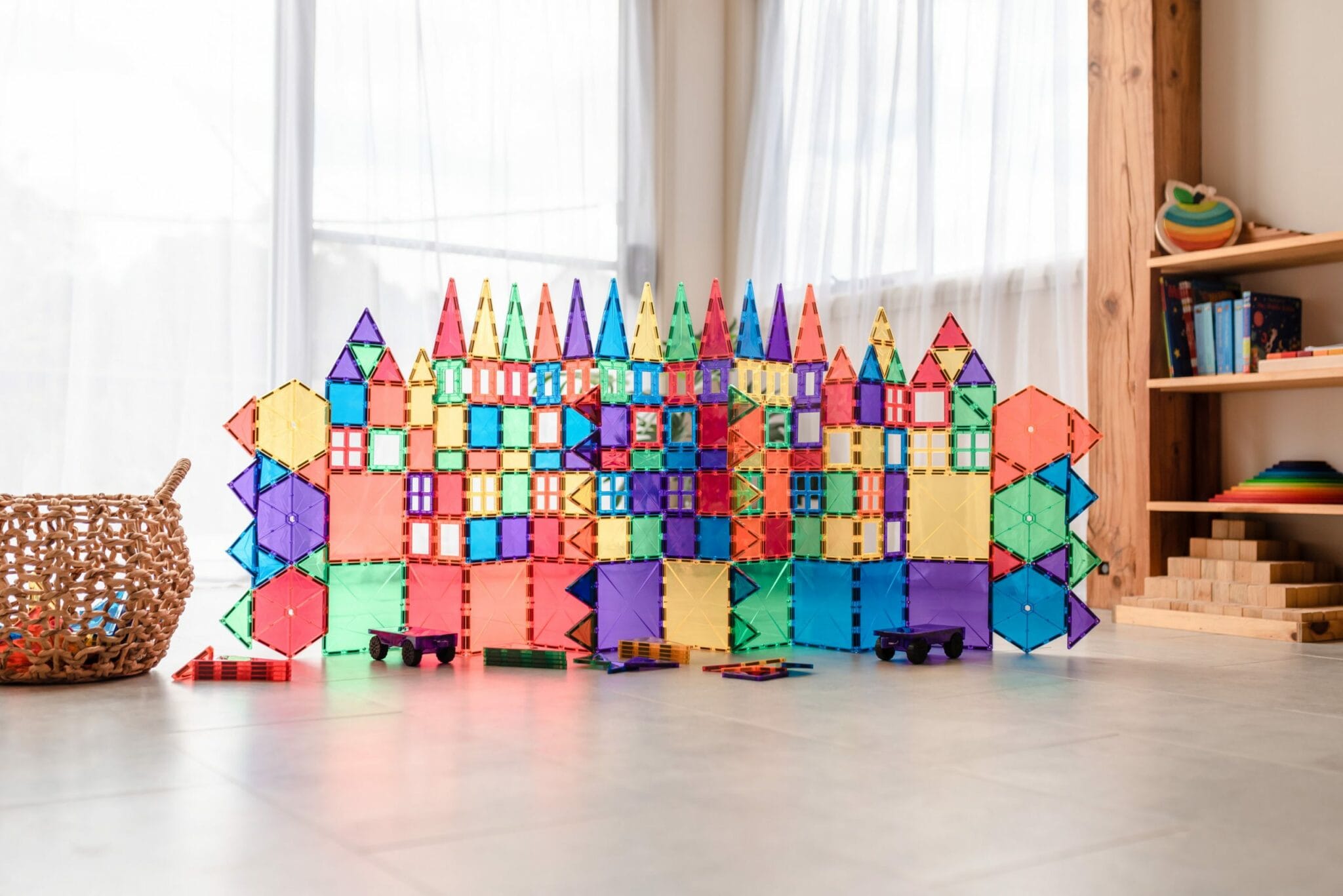Cidade colorida e complexa construída com blocos magnéticos Connetix transparentes, incluindo casas e veículos, em sala de estar.