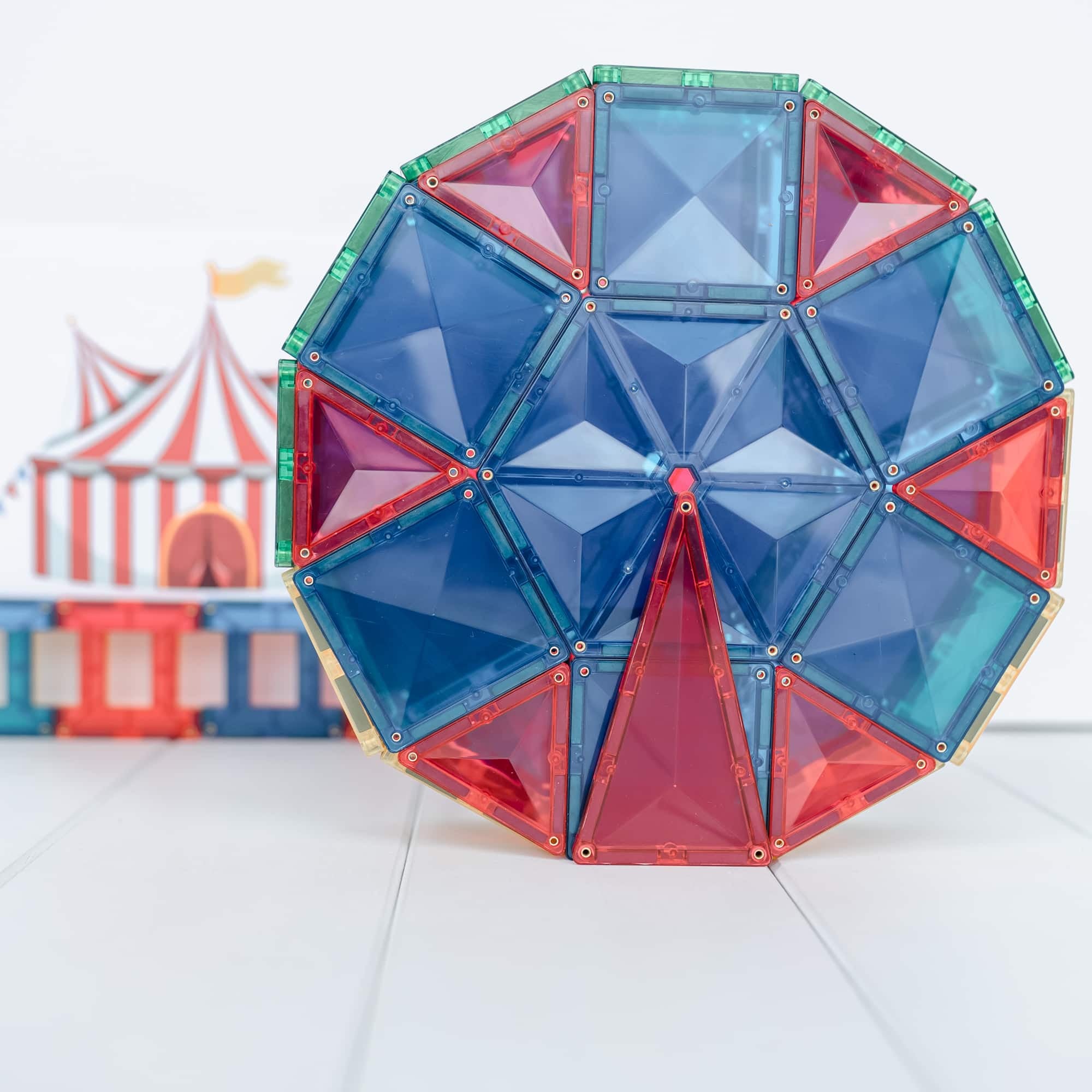 Roda gigante colorida construída com blocos magnéticos Connetix transparentes, com um circo desfocado ao fundo.