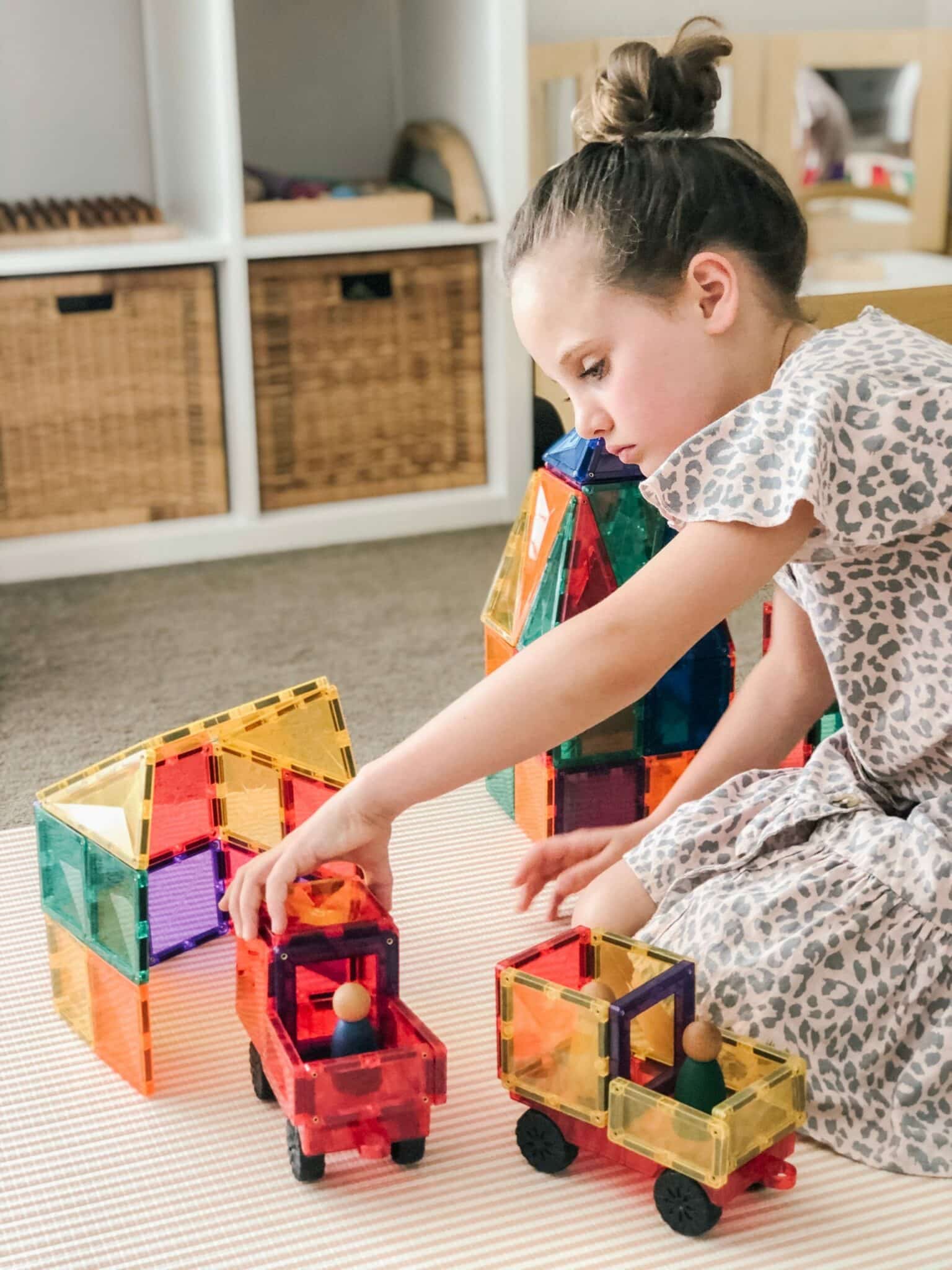 Menina a construir veículos com blocos magnéticos Connetix Motion perto de uma estrutura maior feita com Connetix, demonstrando o jogo criativo.