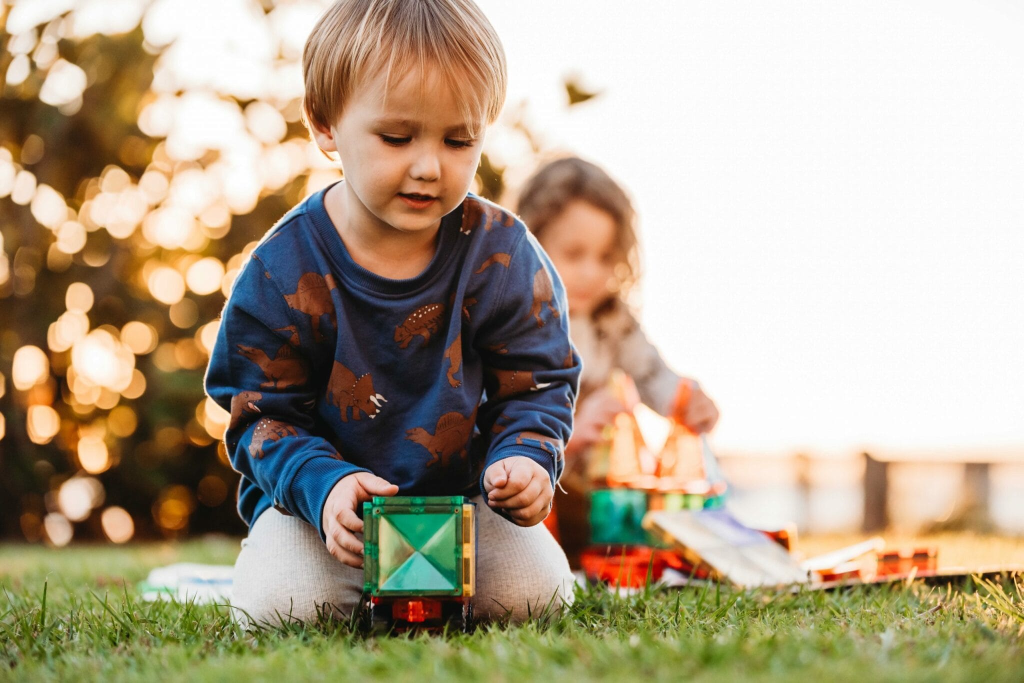 Criança pequena a focar-se na construção de um veículo com blocos magnéticos Connetix Motion no exterior, com outra criança ao fundo.