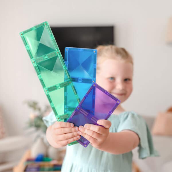 Criança sorridente a segurar vários blocos magnéticos retangulares Connetix translúcidos nas cores verde, azul e roxo.
