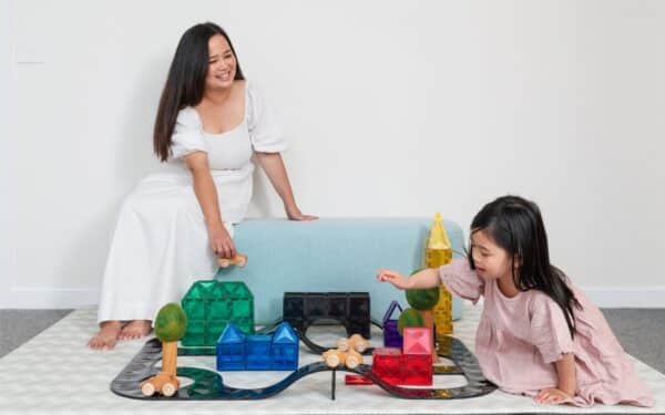 Mãe e criança brincam juntas no chão com o Roads Pack 48 da Connetix, construindo uma cidade com rampas e blocos magnéticos coloridos.
