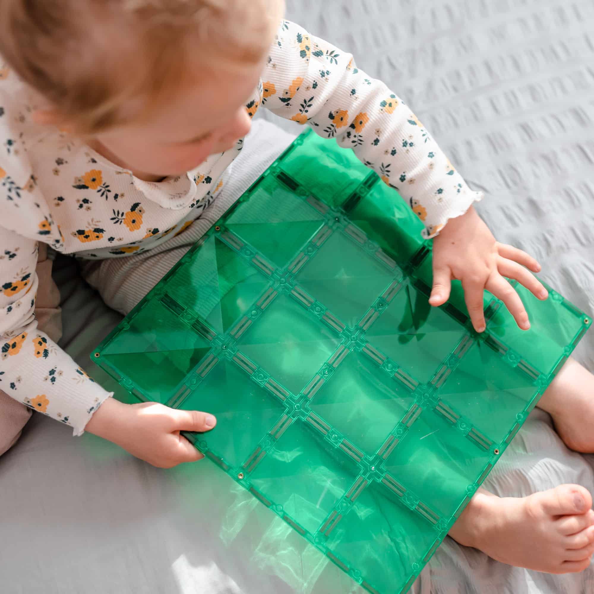 Bebê brincando com a placa base magnética Connetix verde. Jogo educativo e divertido para crianças.