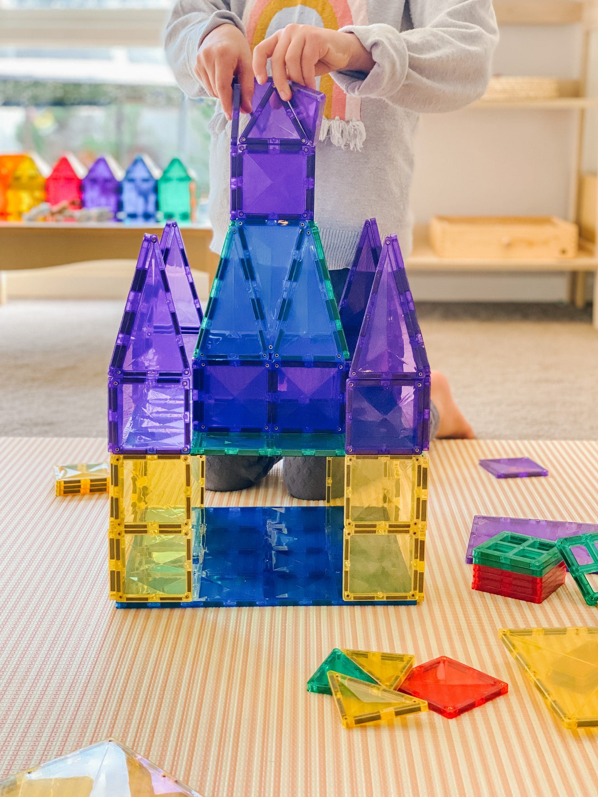Criança brincando com Connetix, construindo um castelo com as peças magnéticas coloridas. Jogo educativo e divertido.
