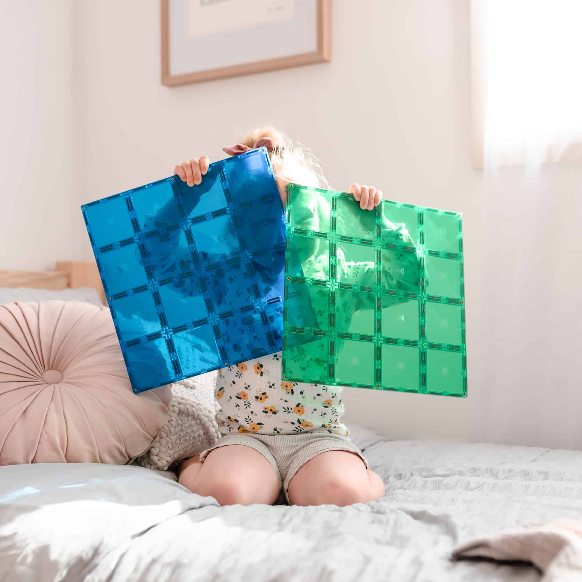 Criança segurando placas base Connetix azul e verde. Jogo magnético educativo para crianças.
