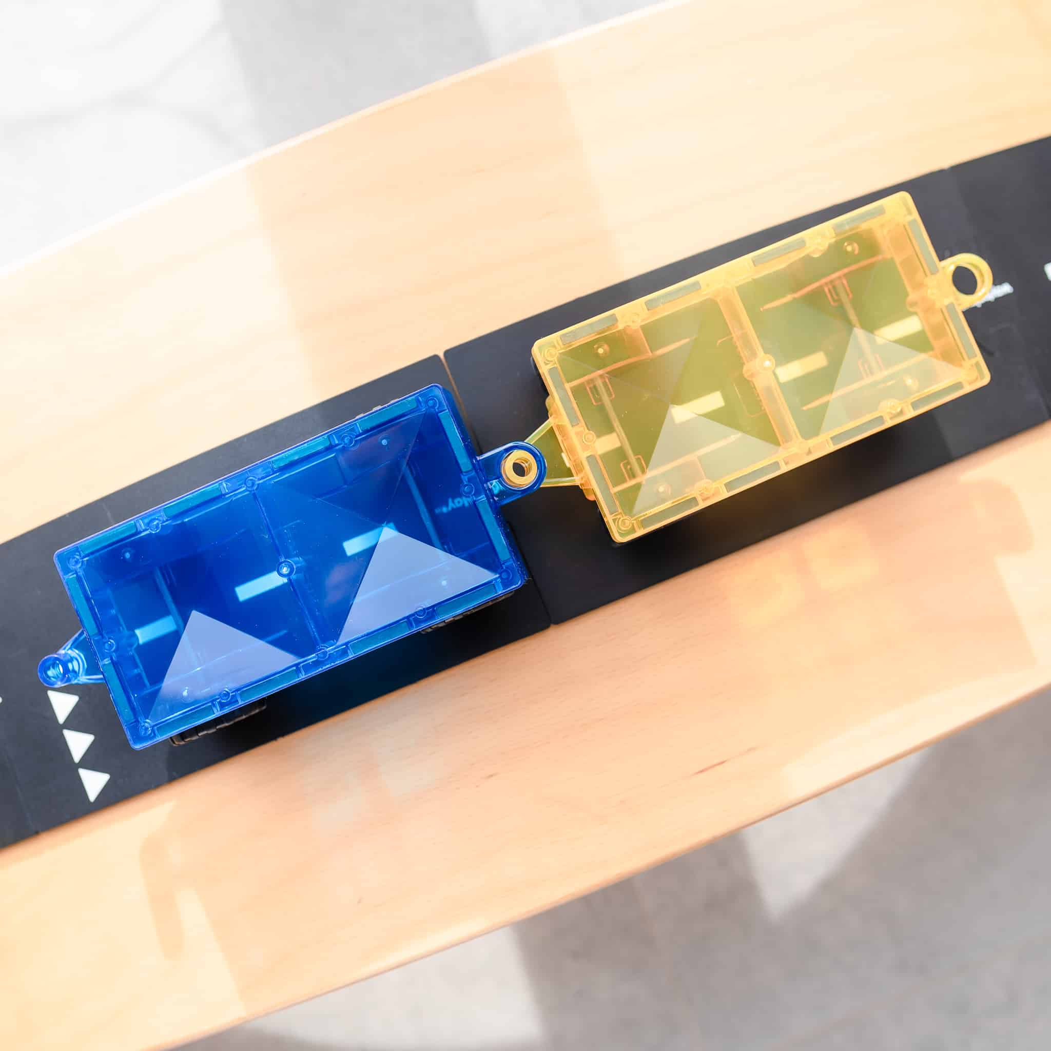 Vista superior dos carros magnéticos Connetix azul e amarelo, conectados. Brinquedo educativo.