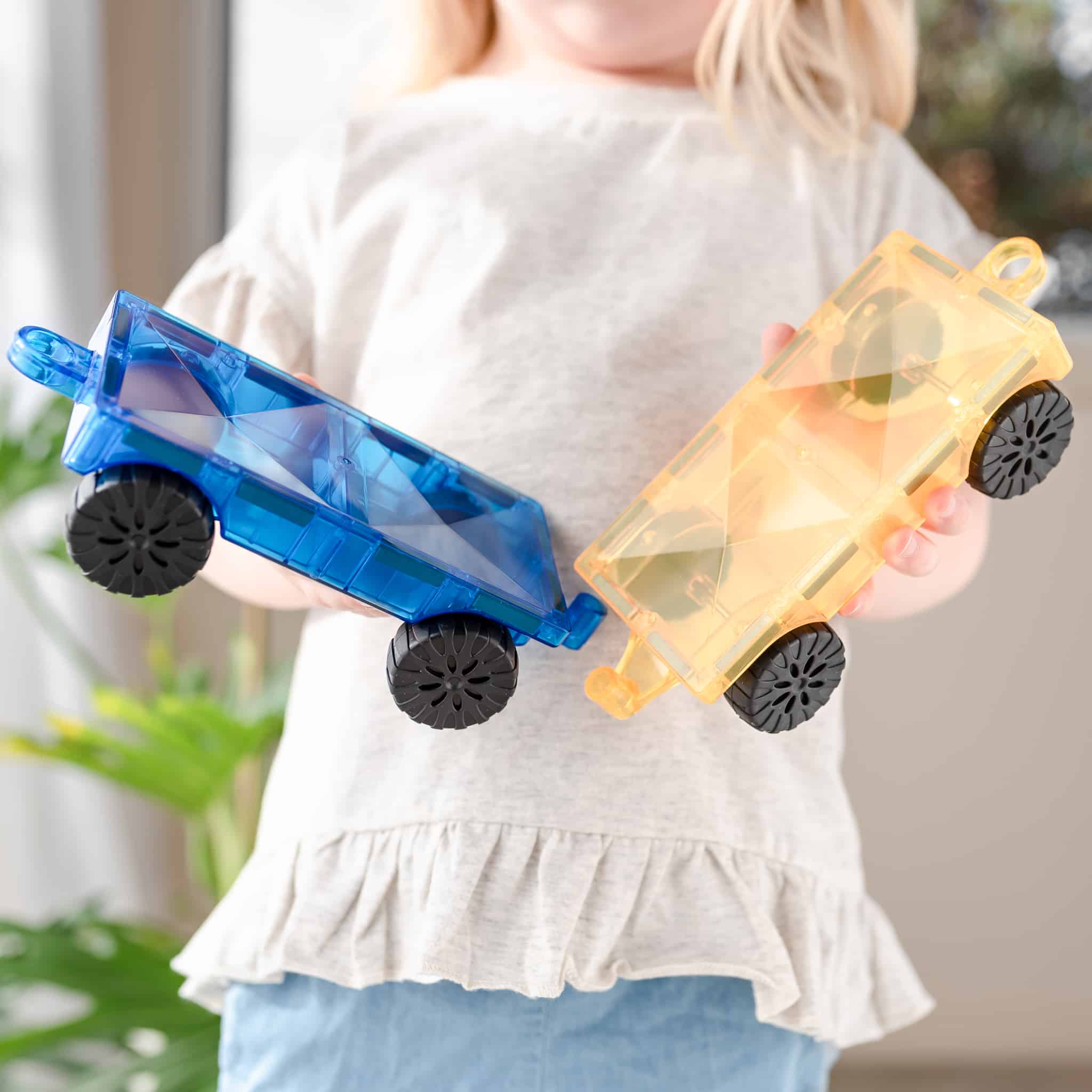 Criança segurando os carros magnéticos Connetix azul e amarelo. Brinquedo educativo e divertido.