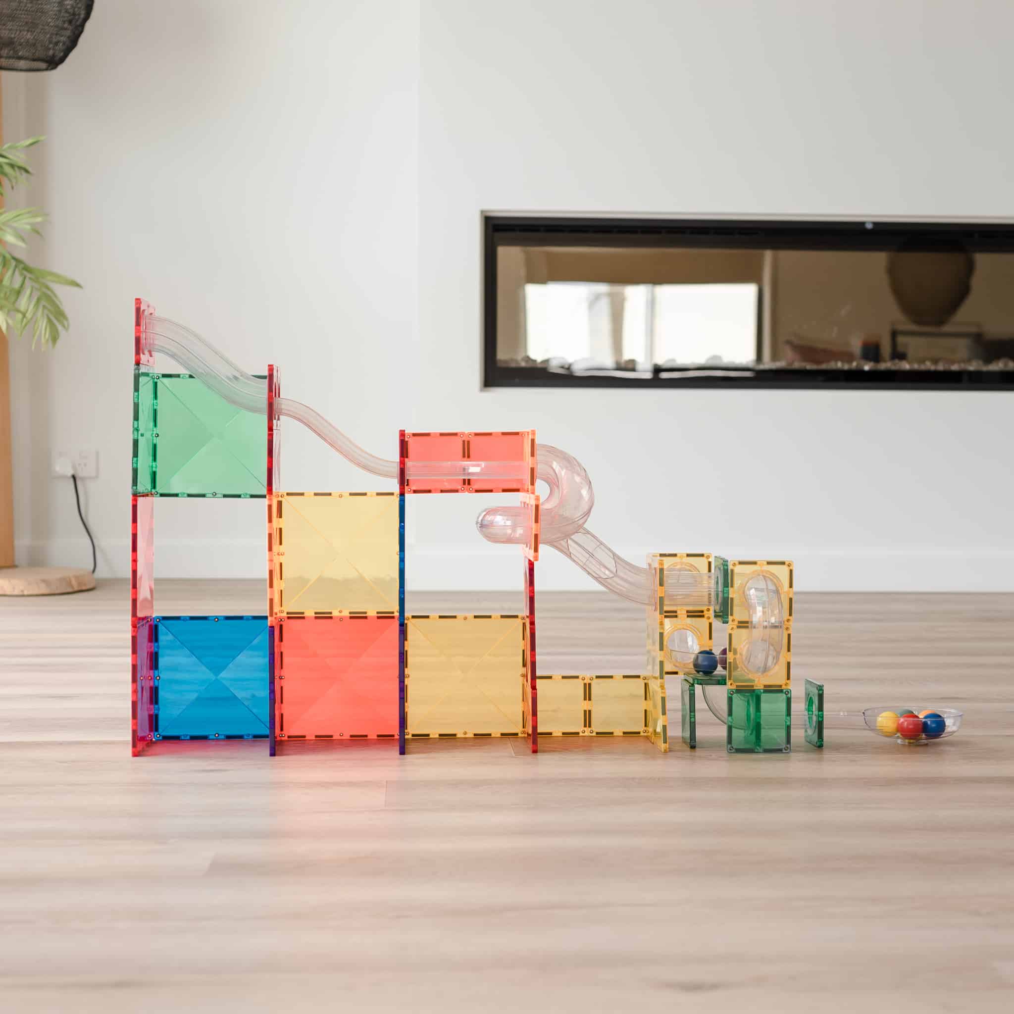 Grande estrutura de Connetix Ball Run Rainbow Expansion construída com blocos magnéticos e tubos em sala.