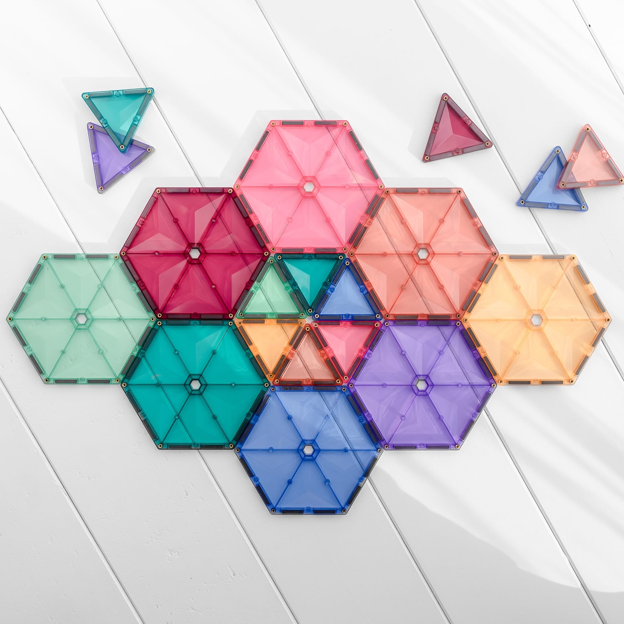 Padrão geométrico com hexágonos e triângulos magnéticos Connetix pastel em fundo de madeira branca.