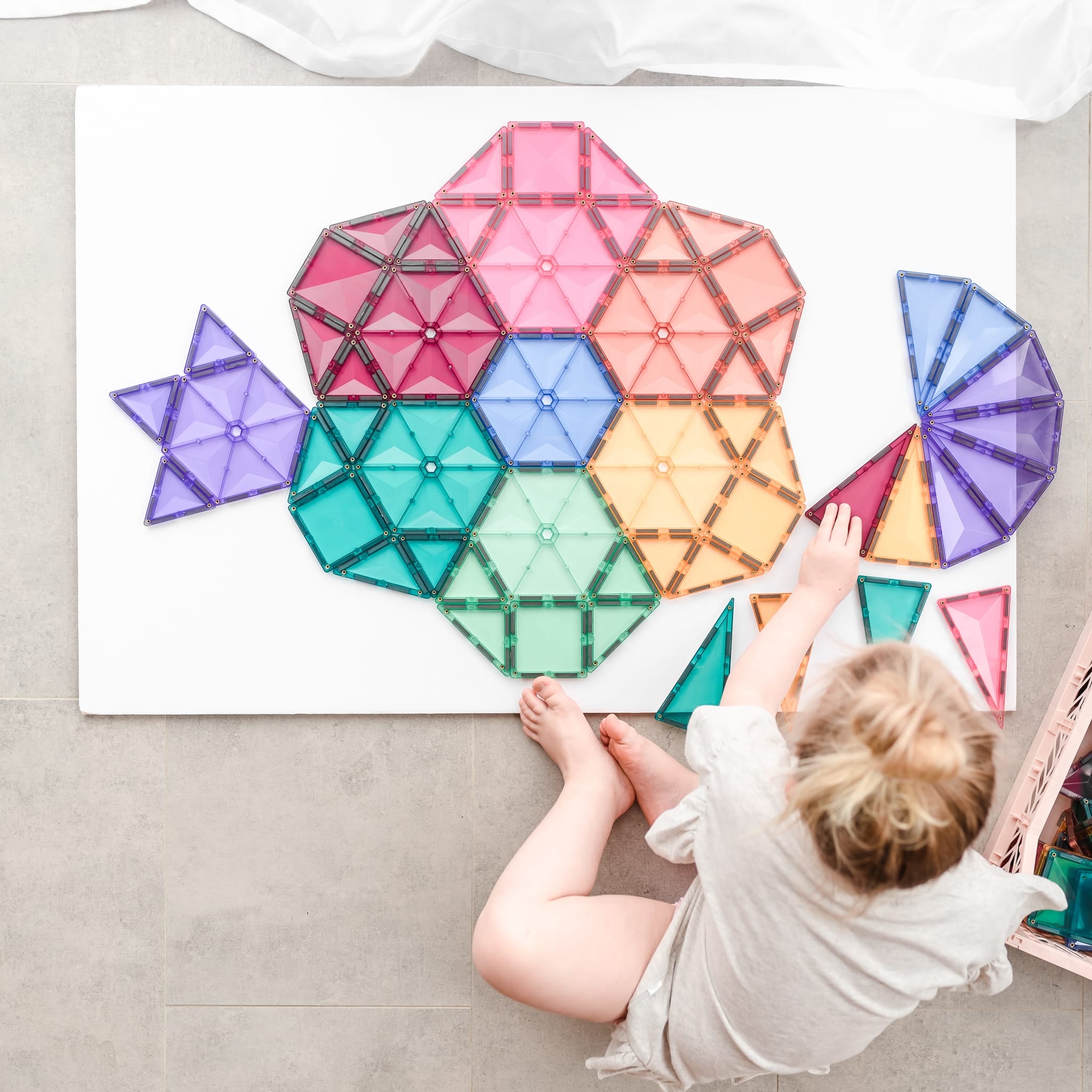 Criança a brincar com blocos magnéticos Connetix Pastel, construindo um peixe no chão.