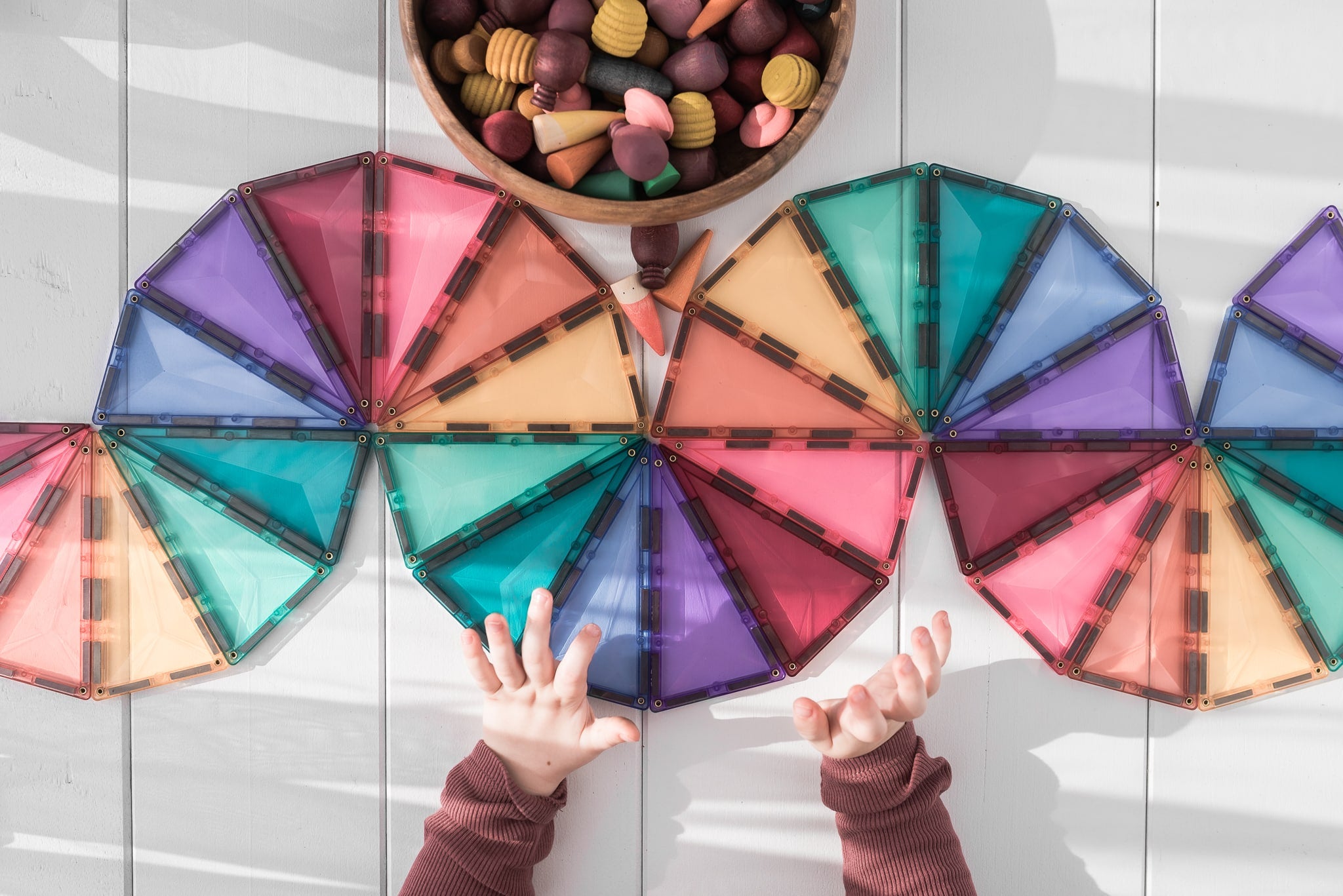 Mãos de criança a interagir com um padrão de blocos magnéticos Connetix Pastel hexagonais e triangulares.
