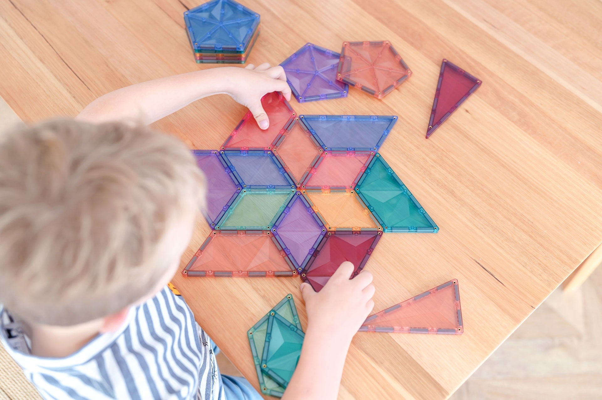 Mãos de criança organizando blocos magnéticos Connetix Pastel Shape Expansion Pack numa mesa.