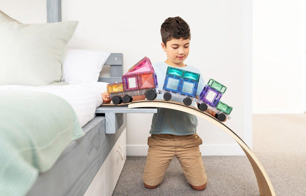 Criança a brincar com um comboio Connetix Pastel Transport numa prancha curva.