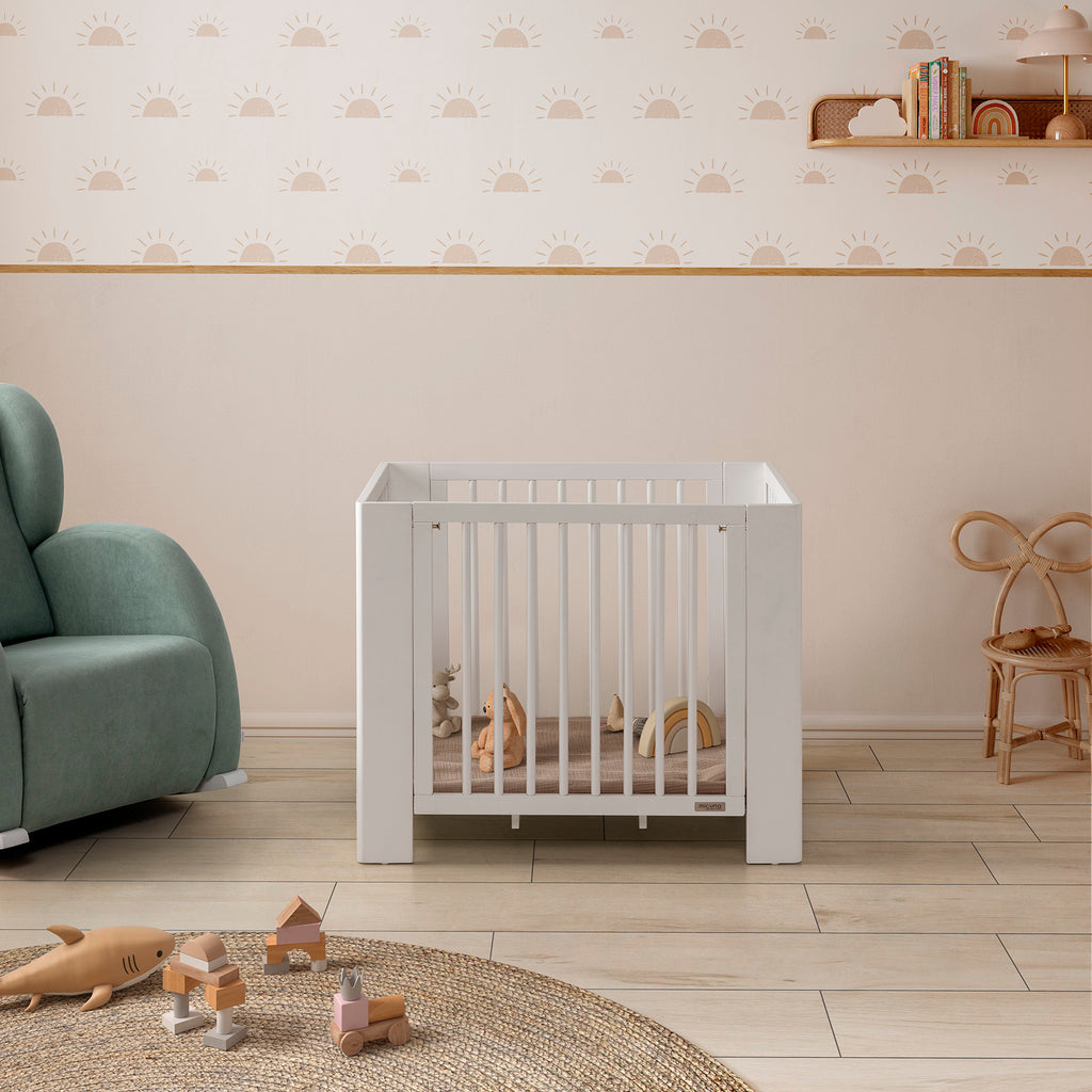 Mini-berço Converbaby 90x50 em quarto de bebé, com brinquedos, ao lado de poltrona e cadeira.