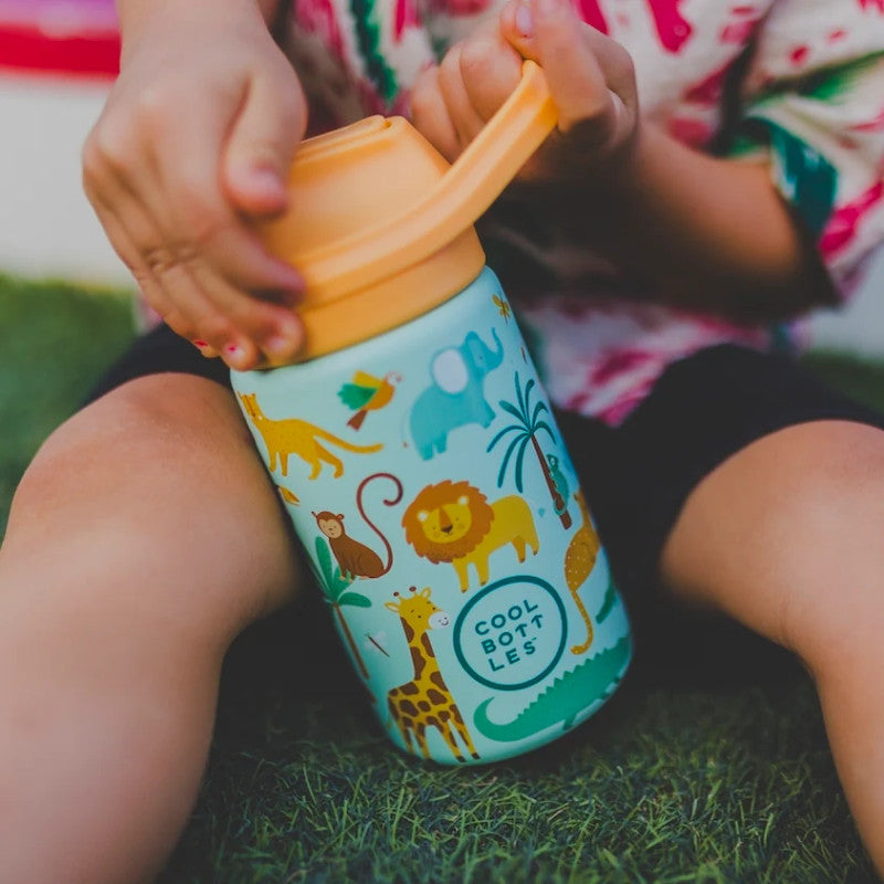 Criança sentada na relva a segurar a garrafa térmica Cool Bottles Wild Crew de 350ml, mostrando o design de animais da selva e a pega integrada.