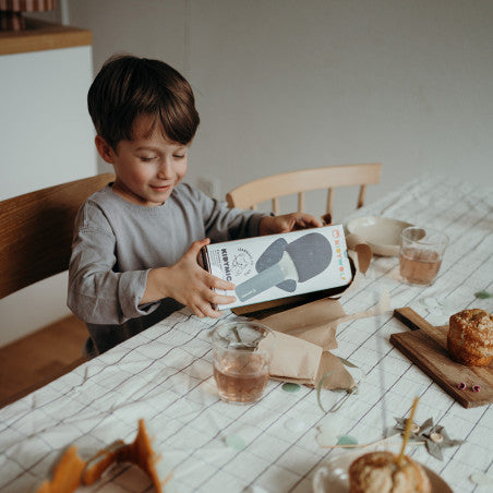 Criança a abrir a caixa do Microfone de Karaoke KidyWolf KIDYMIC numa mesa com toalha listrada.