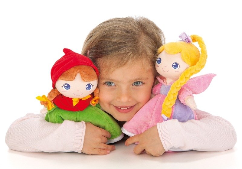 Criança sorridente a brincar com dois peluches Trudi Princesas: o Capuchinho Vermelho e uma fada de cabelo amarelo.