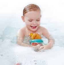 Criança sorridente a brincar alegremente com o Hape Ursinho nadador na banheira com espuma.