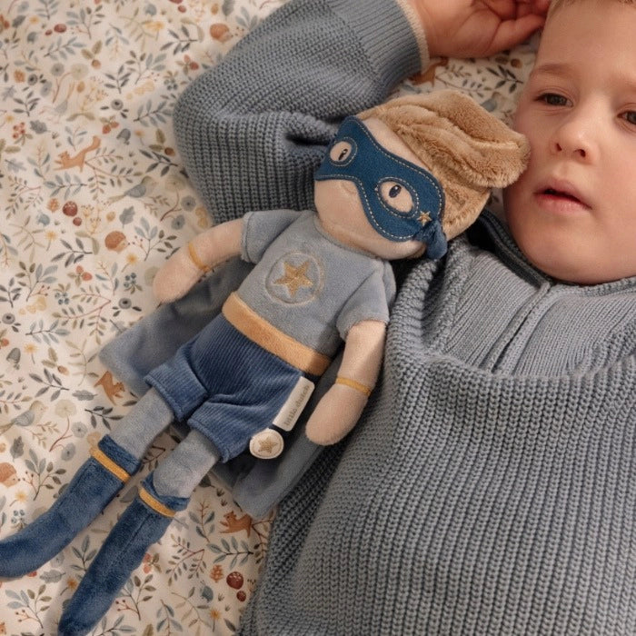 Criança deitada a descansar com o Peluche Super-herói Jim ao lado, demonstrando a função de conforto do brinquedo.