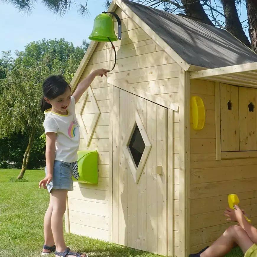 Criança a instalar a campainha verde do kit de acessórios Soulet numa casinha de madeira, promovendo interação e diversão.