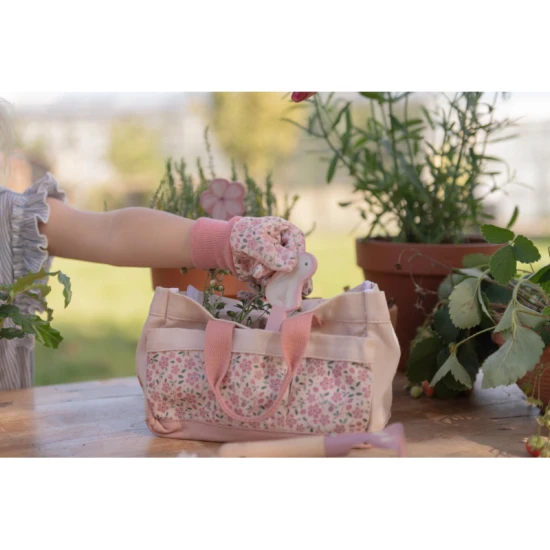 Uma criança com luvas de jardinagem cor-de-rosa a colocar uma ferramenta na bolsa de transporte do kit Little Dutch Fairy Garden.