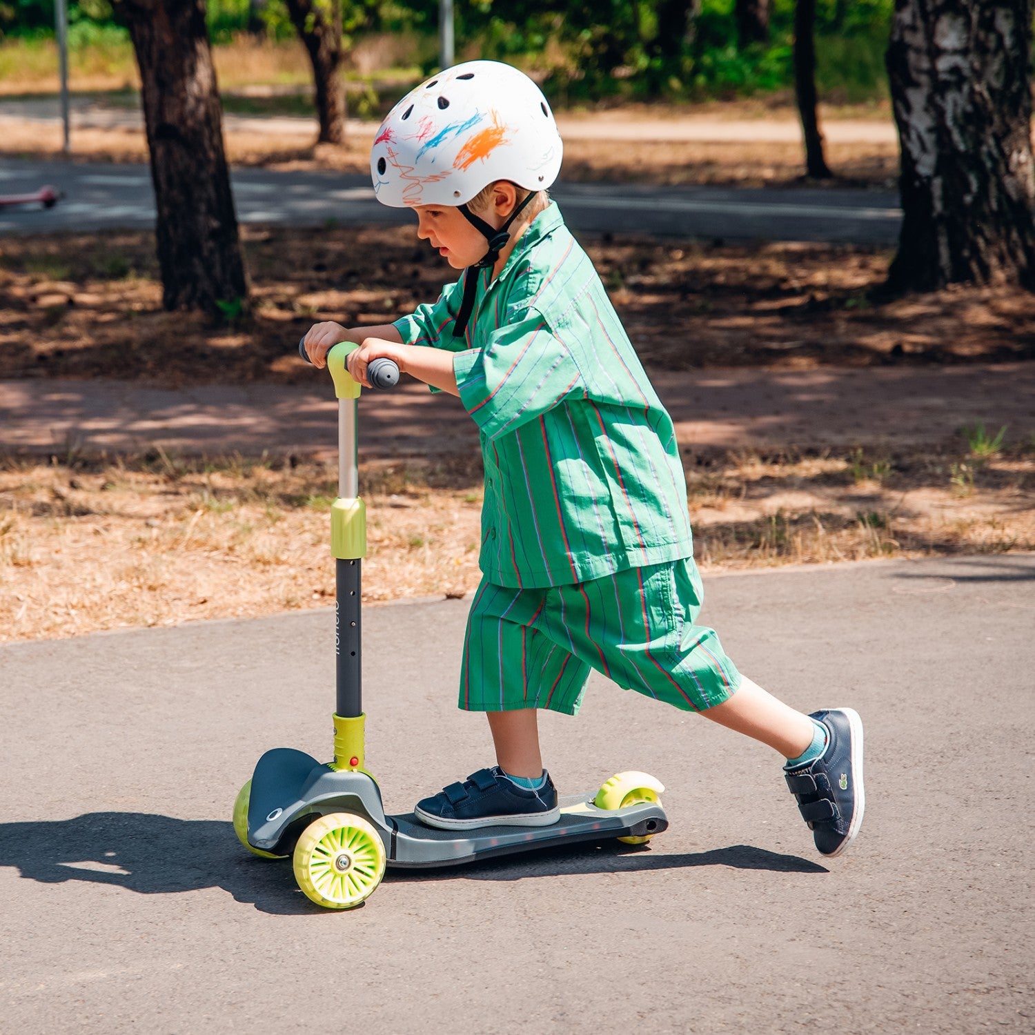 Criança com capacete a andar na trotinete Lionelo Timmy de 3 rodas num passeio pavimentado, demonstrando uso ativo.