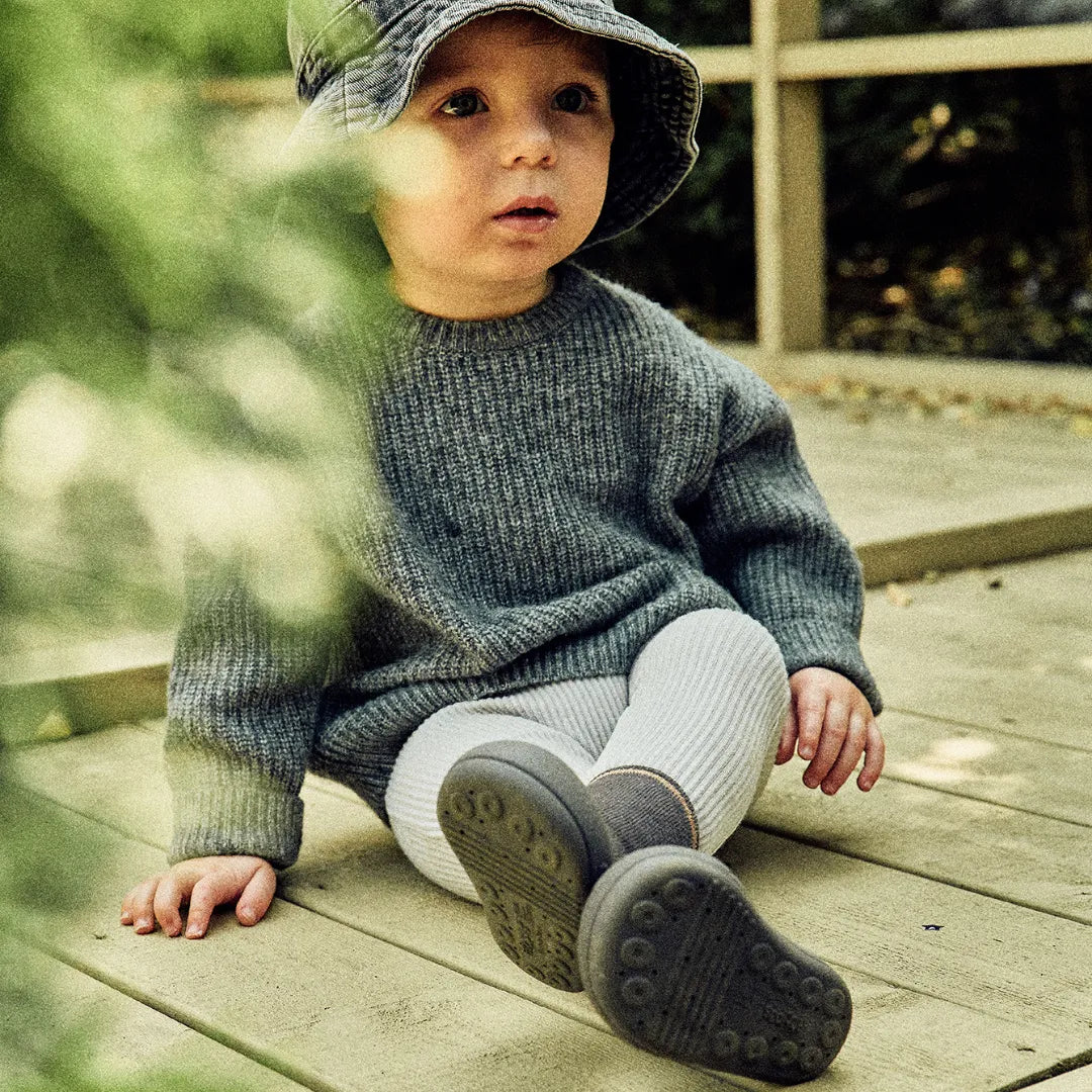 Criança sentada num deck de madeira, vestindo roupa confortável e calçando Attipas Shiny Star Charcoal, destacando o ajuste ergonómico.