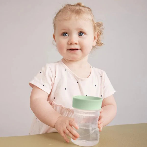 Criança pequena a segurar e a beber do copo de treino b.box com tampa verde menta.