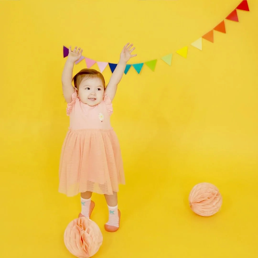 Criança pequena a brincar com bolas coloridas enquanto usa Attipas Peekaboo Peach, calçado barefoot com riscas rosa e branco.