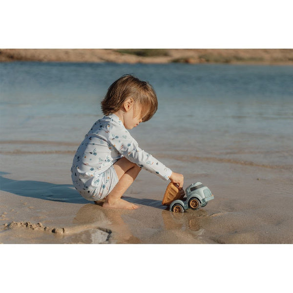 Criança pequena a brincar com o camião de reboque Little Dutch na areia molhada junto à água.