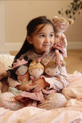 Criança sorridente a segurar várias bonecas de peluche, incluindo a Super-Heroína Rosa, num ambiente acolhedor.