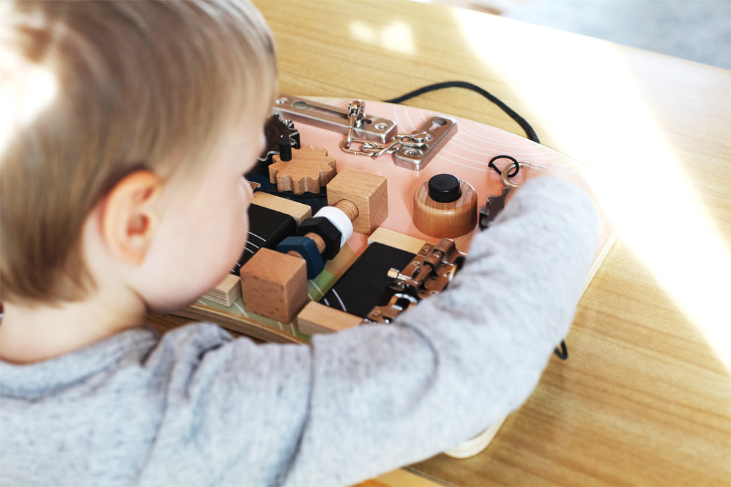 Criança pequena interagindo com o quadro de atividades small foot, demonstrando o uso intuitivo e divertido dos diferentes mecanismos.