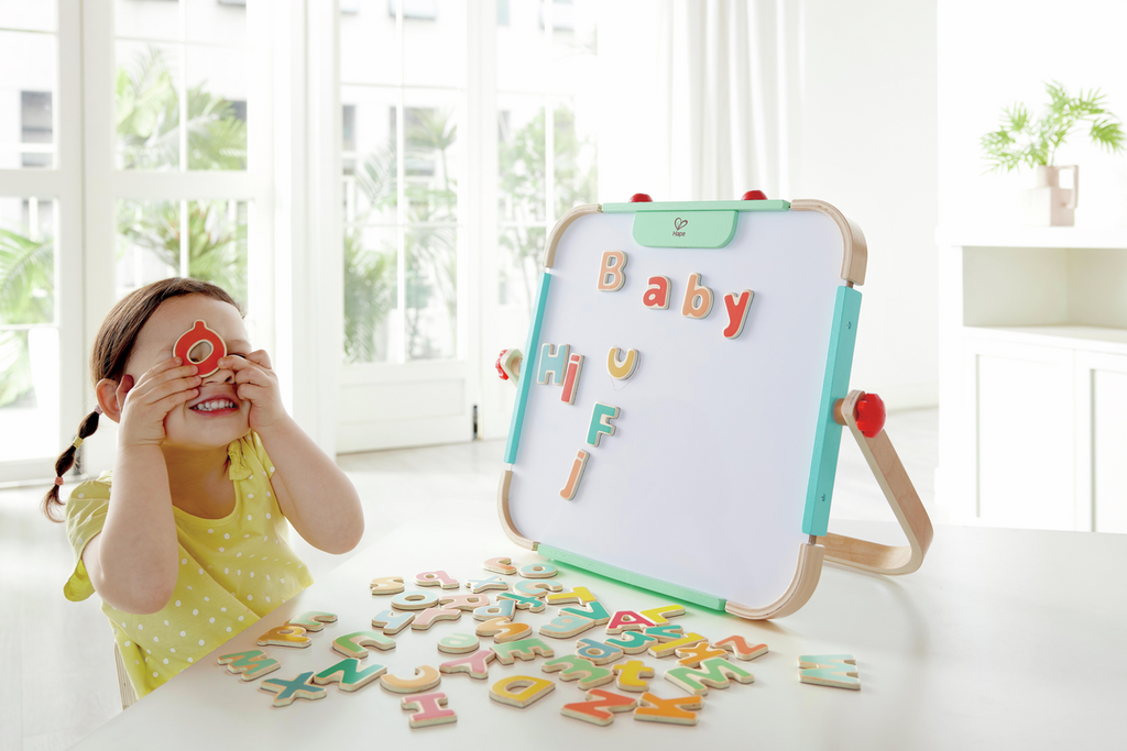 Criança a brincar com letras magnéticas Hape num quadro branco.