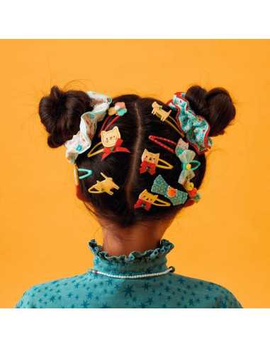 Criança com o cabelo penteado em duas marias, decorado com várias barrettes coloridas de gatos e laços da Djeco, em destaque contra um fundo laranja.