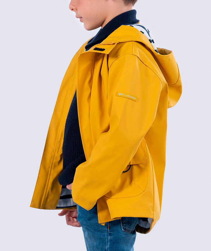 Vista lateral de uma criança a usar o casaco de chuva amarelo Igor, mostrando o corte e a etiqueta da marca na manga.