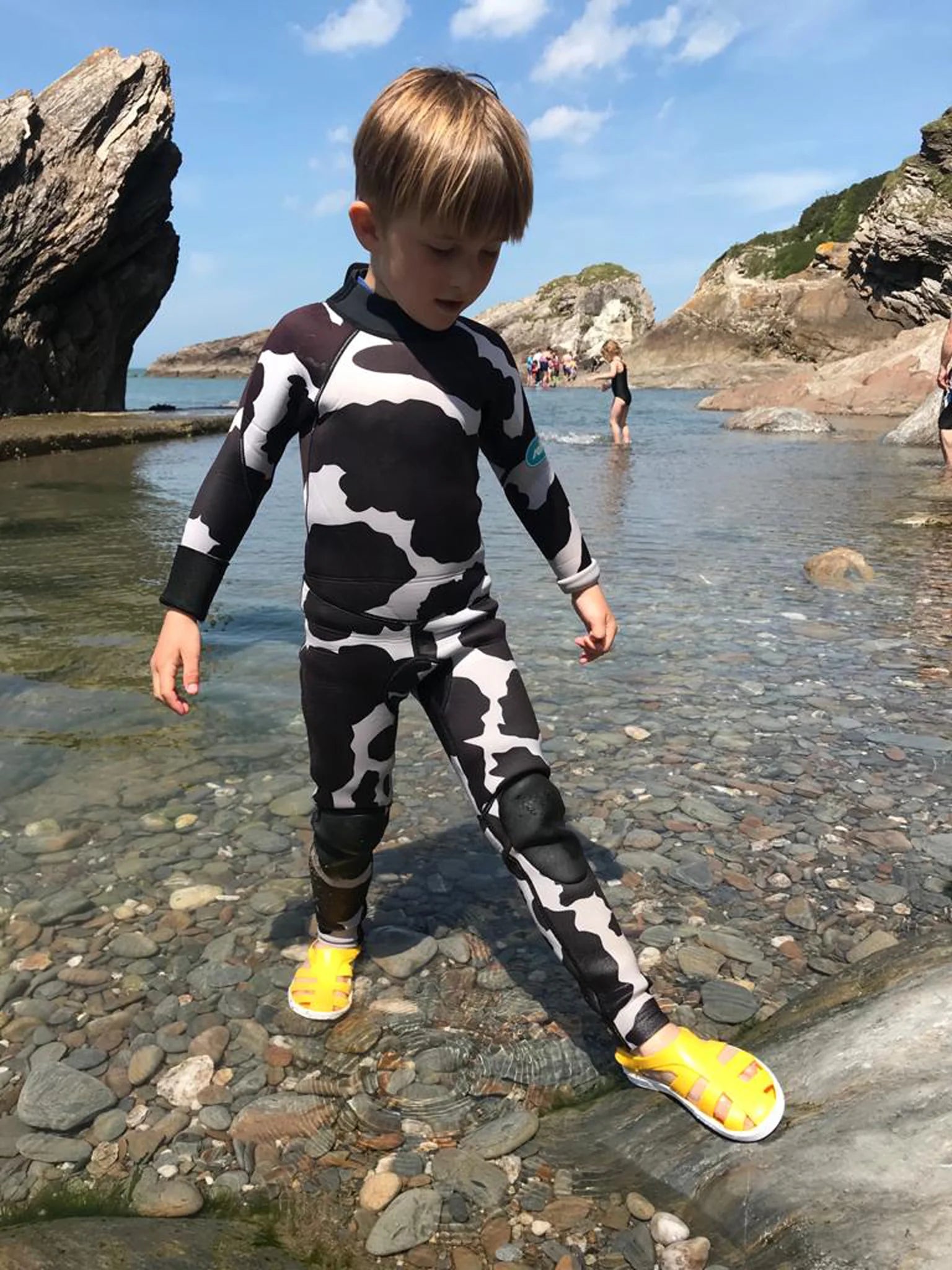 Criança a usar sandálias Boatilus Bioty amarelas a brincar na água na praia.