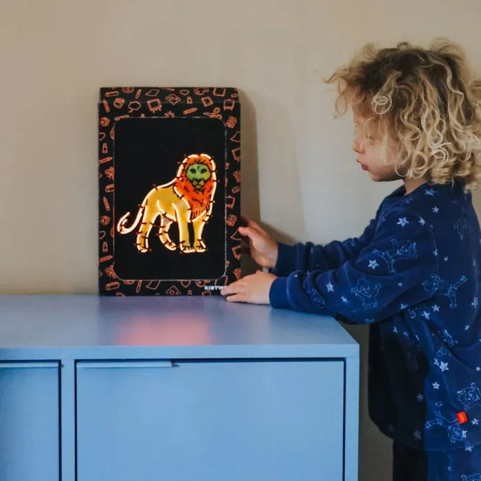 Criança a observar um quadro de leão iluminado com neon laranja em cima de um móvel azul.