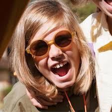 Criança sorridente a usar os óculos de sol Ki ET LA WOAM mostarda, em ambiente exterior, demonstrando o uso prático.