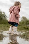 Criança com galochas Little Dutch brancas com padrão floral a caminhar numa poça de água, diversão em dias de chuva.