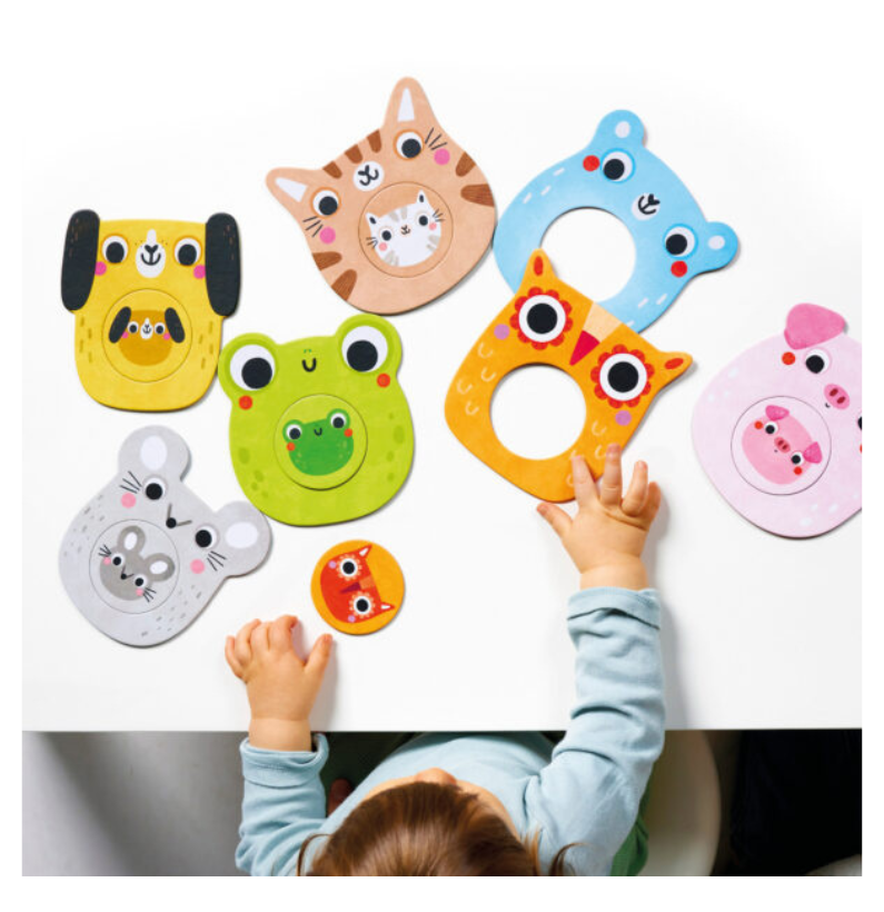 Mãos de uma criança a montar os 7 puzzles de animais do Banana Panda Mini Me espalhados numa mesa branca.