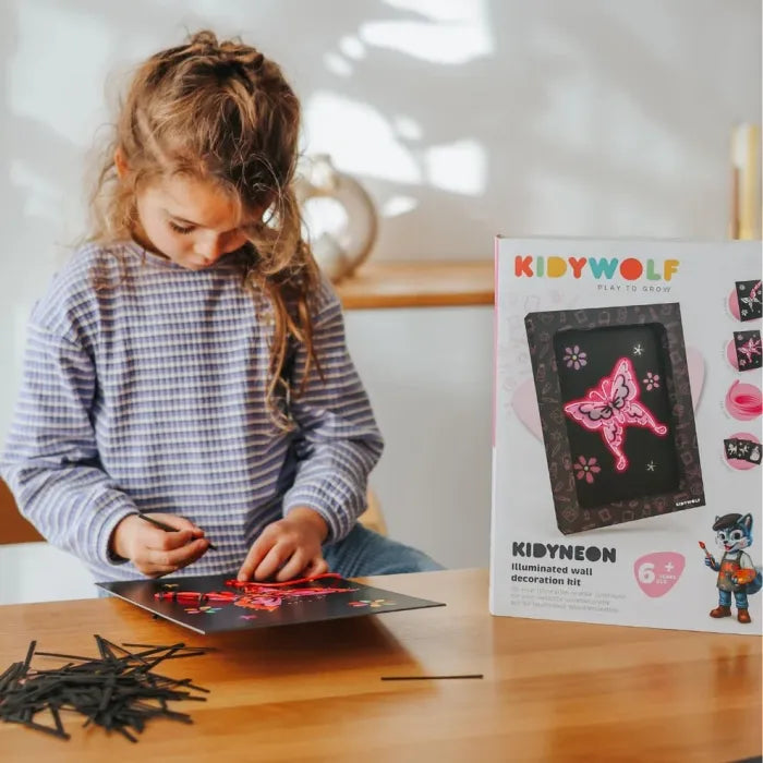 Menina sentada à mesa a montar o seu kit Kidyneon, inserindo os fios na placa de cartão preta.