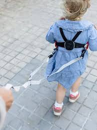 Criança pequena a caminhar com arnês de segurança Trunki preso a uma mão adulta.