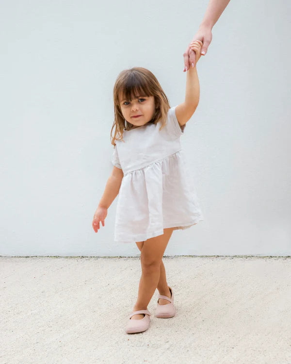 Criança pequena a caminhar, segurando a mão de um adulto, usando sapatilhas barefoot rosa.