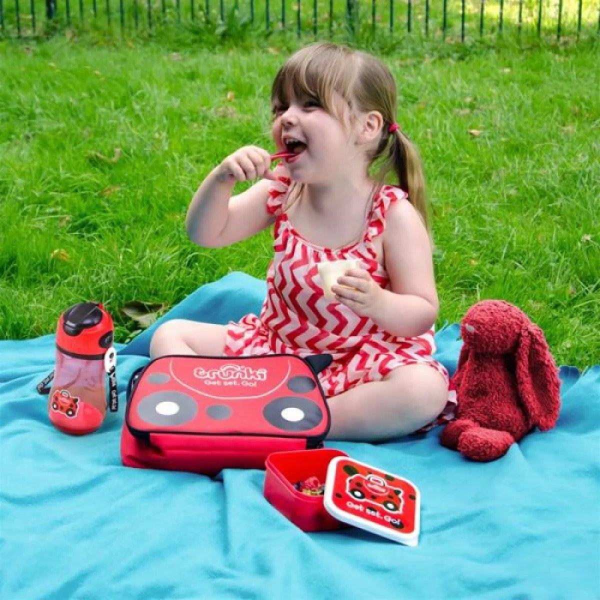 Criança feliz num piquenique ao ar livre utilizando a lancheira Trunki Harley Mariquita.