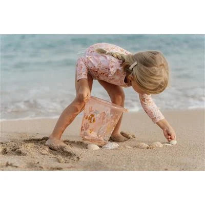 Criança inclinada a apanhar conchas do chão da praia, segurando o balde cor de rosa da Little Dutch.