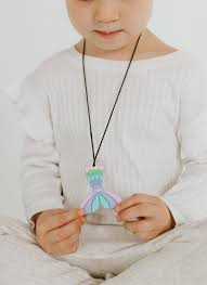 Criança de camisola branca a segurar o colar sensorial Jellystone com o pendente em forma de cauda de sereia em tons pastel.