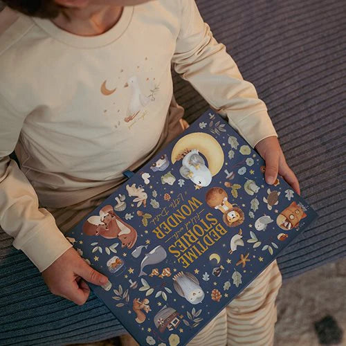 Criança a segurar o livro de histórias da Little Dutch com a capa ilustrada por animais noturnos e a lua.