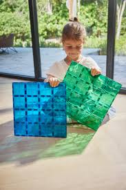 Criança sorridente a segurar as duas placas magnéticas coloridas, azul e verde, prontas para construir.