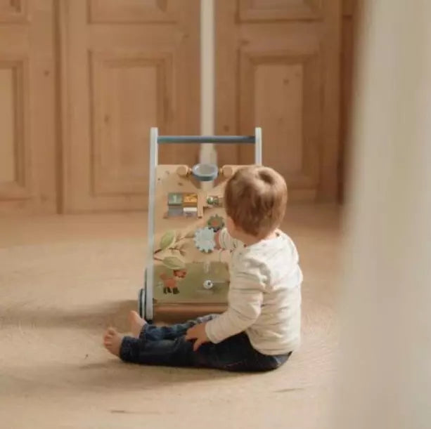 Criança pequena sentada no chão a brincar com o painel de atividades do andarilho Little Dutch.