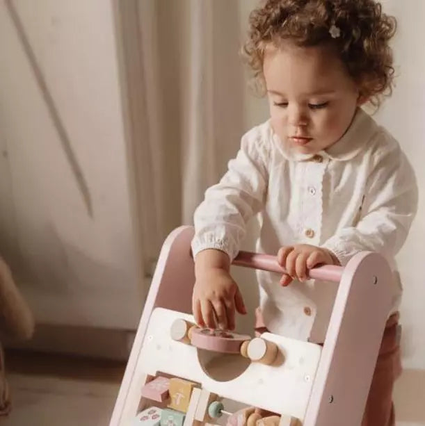 Criança pequena com cabelo encaracolado a empurrar o andarilho de atividades Little Dutch, concentrada em mexer nos brinquedos do painel.